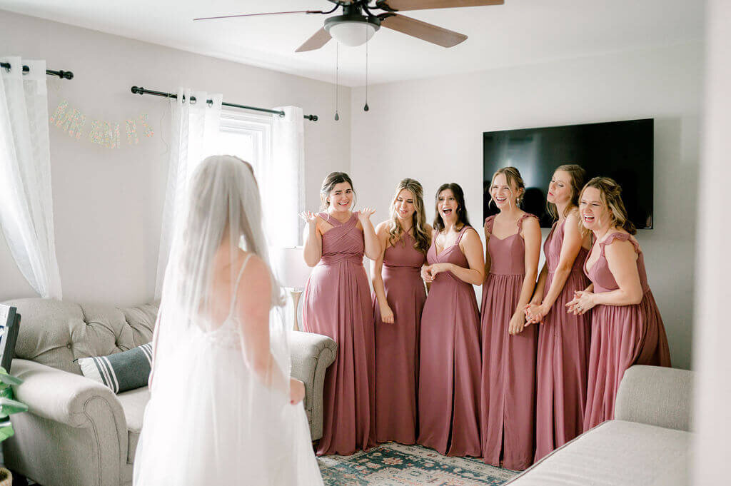 Bridemaids looking excited as they see the bride in her wedding dress for the first time