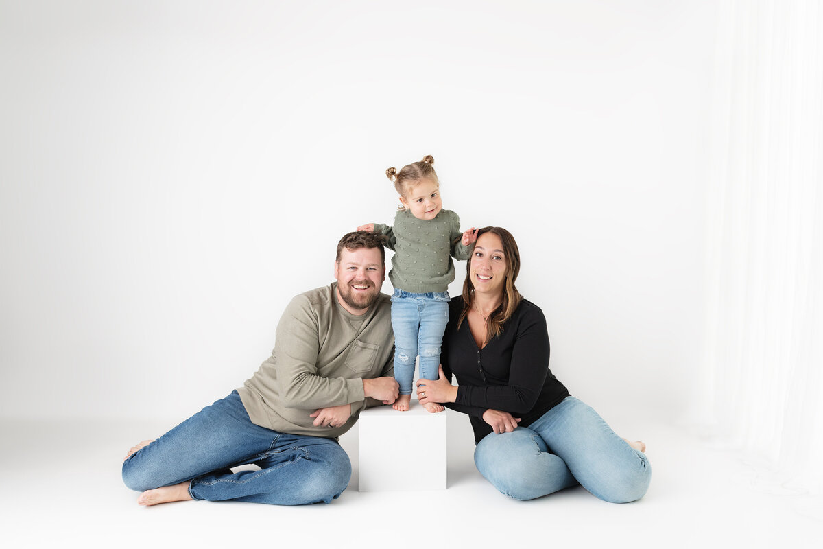 Studio family portrait with daughter standing on white cube between parents | Paris Ontario