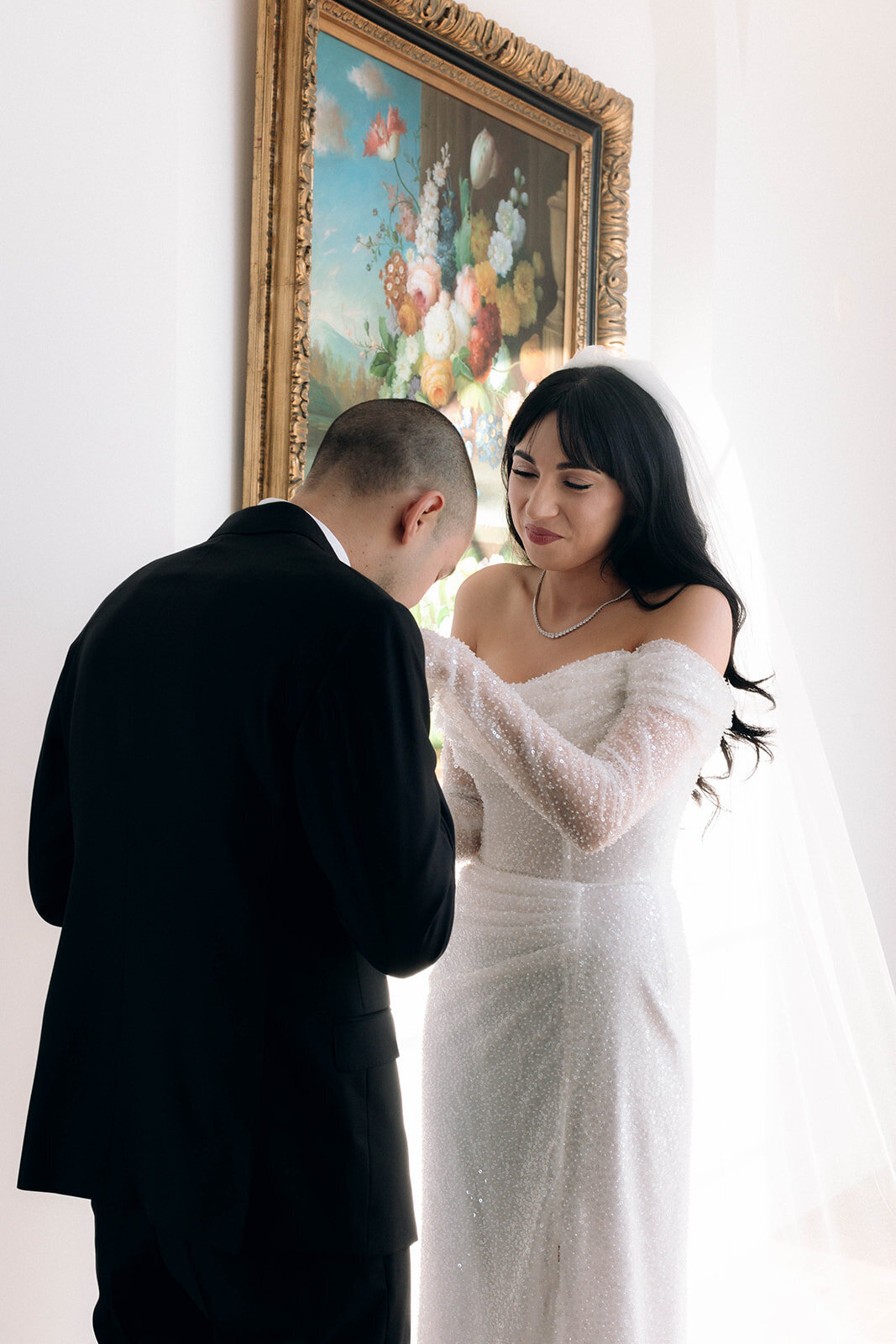 A groom kisses the bride’s hand in an emotional wedding moment, surrounded by soft light and vintage decor. A perfect example of documentary wedding photography with an artistic and editorial touch.