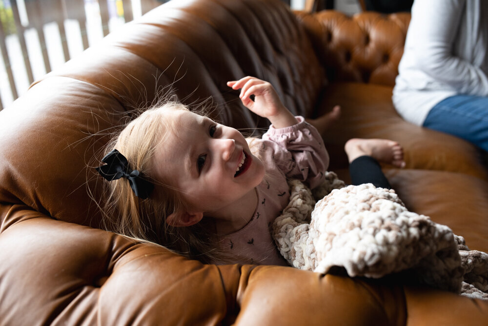 Static hair little girl with blue bow on brown couch