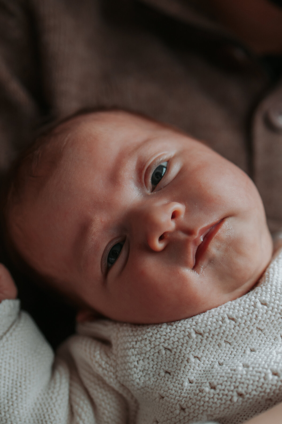 Een baby kijkt omhoog naar de camera met een nieuwsgierige en schattige uitdrukking op zijn gezicht.