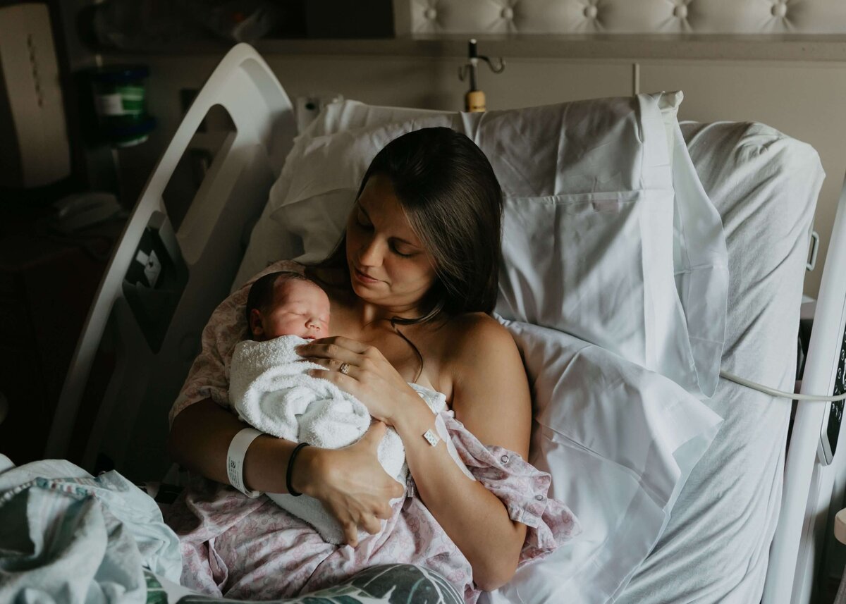 A woman cradling a newborn in a hospital bed, captured by a Pittsburgh newborn photographer.