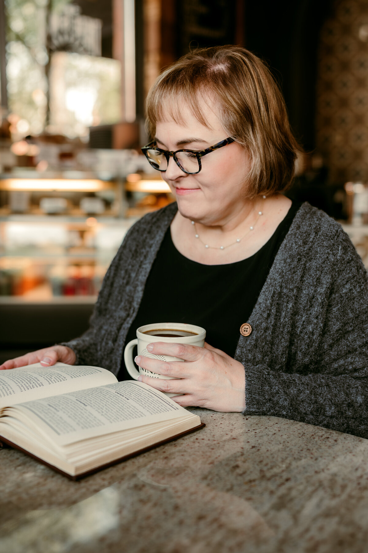 Mature woman reading a book at Nina’s Coffee Café during online dating photo session in St. Paul, MN