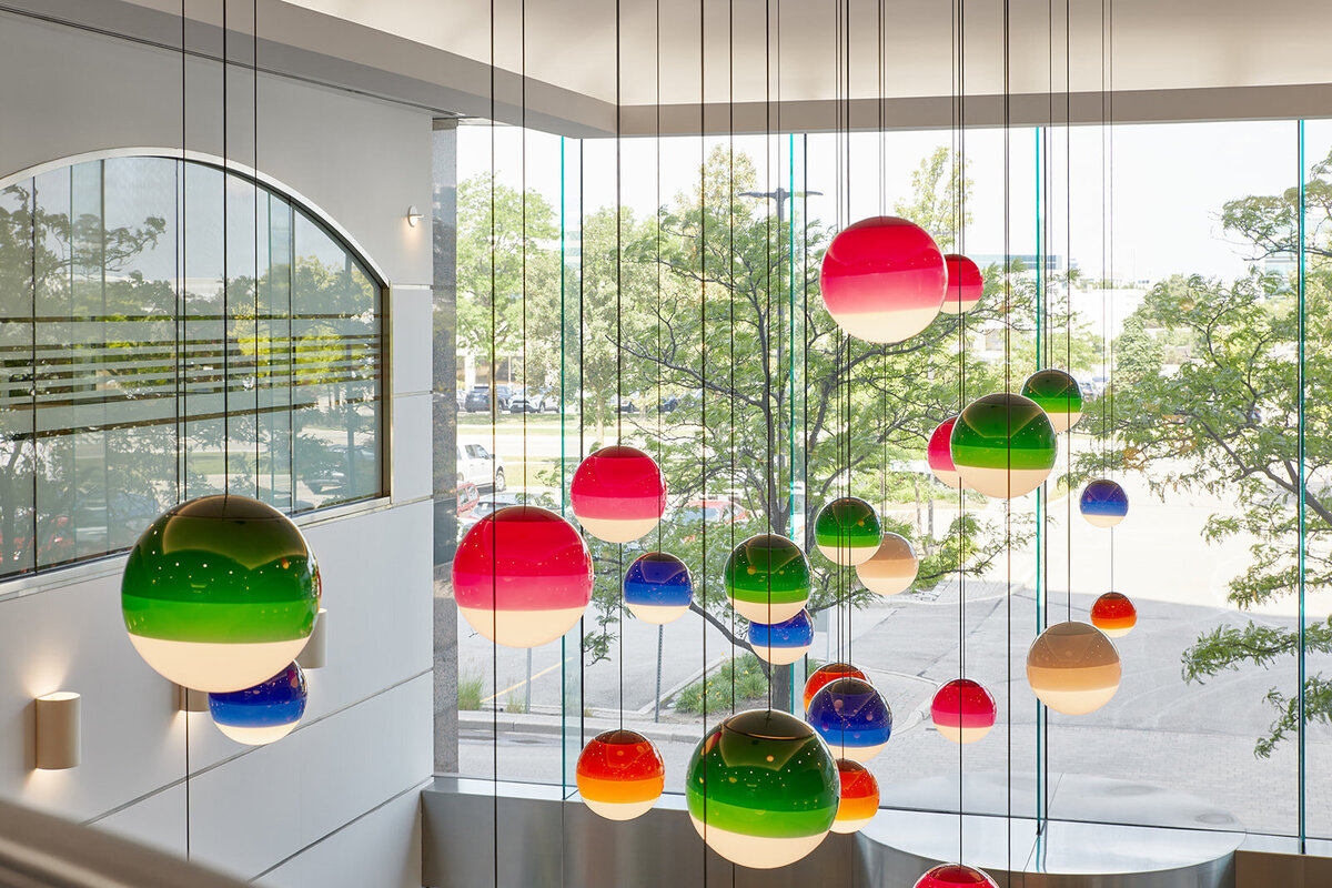 A cluster of tritone globe pendant lights hanging from the ceiling in front of a bright window over looking the lobby entrance