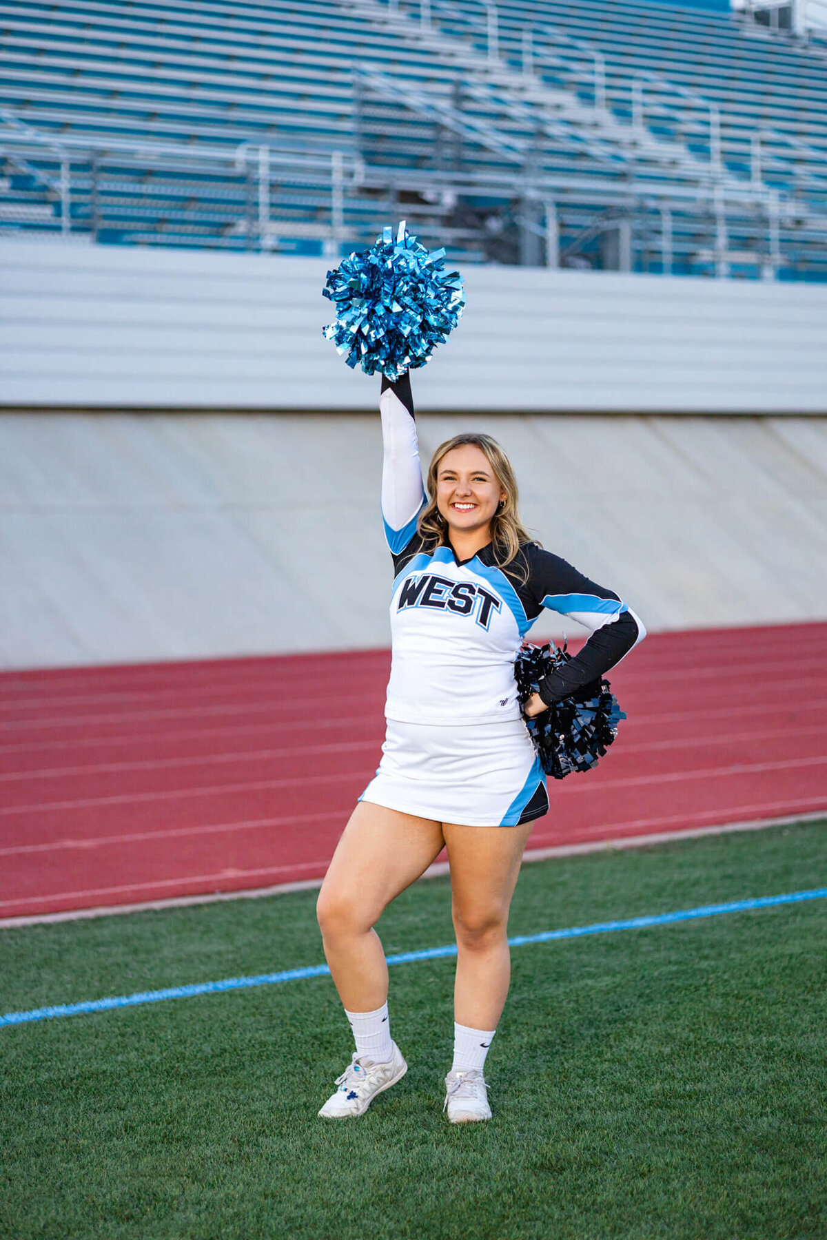 high school senior cheerleader posing on the football field in front of the stadium