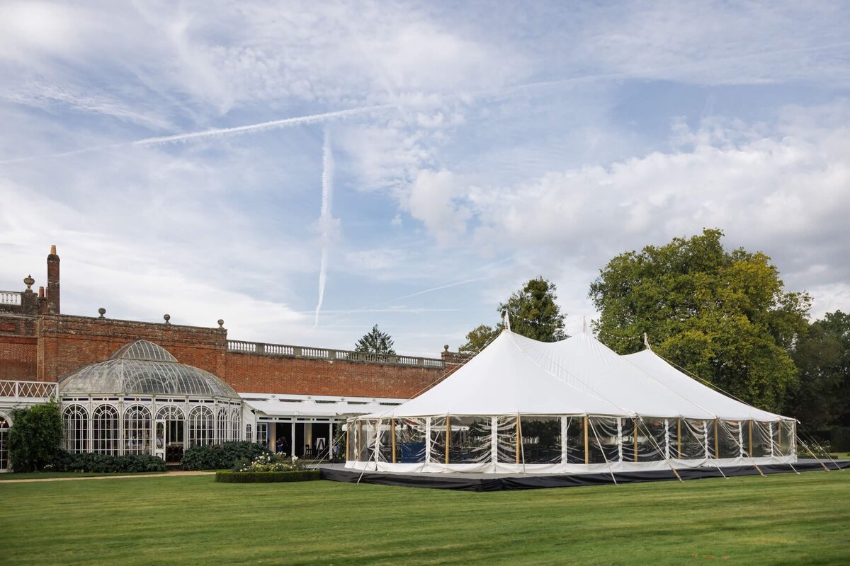 A pole marquee next to a buulding with an orangery attached.