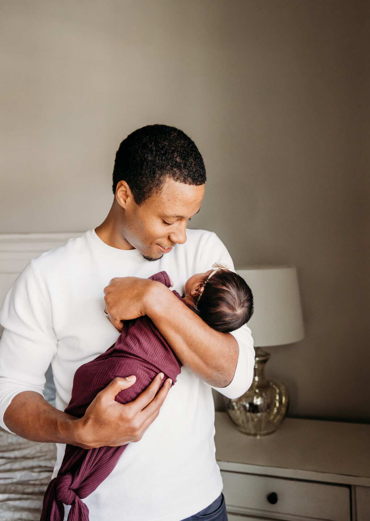 Newborn Photographer, a father smiles as he holds his baby daughter to his chest at home