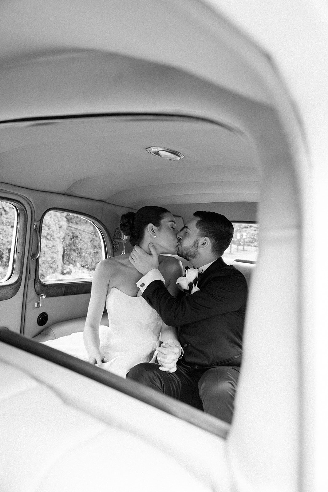 Bride and groom share romantic kiss in the back of a vintage car parked on Long Island. 