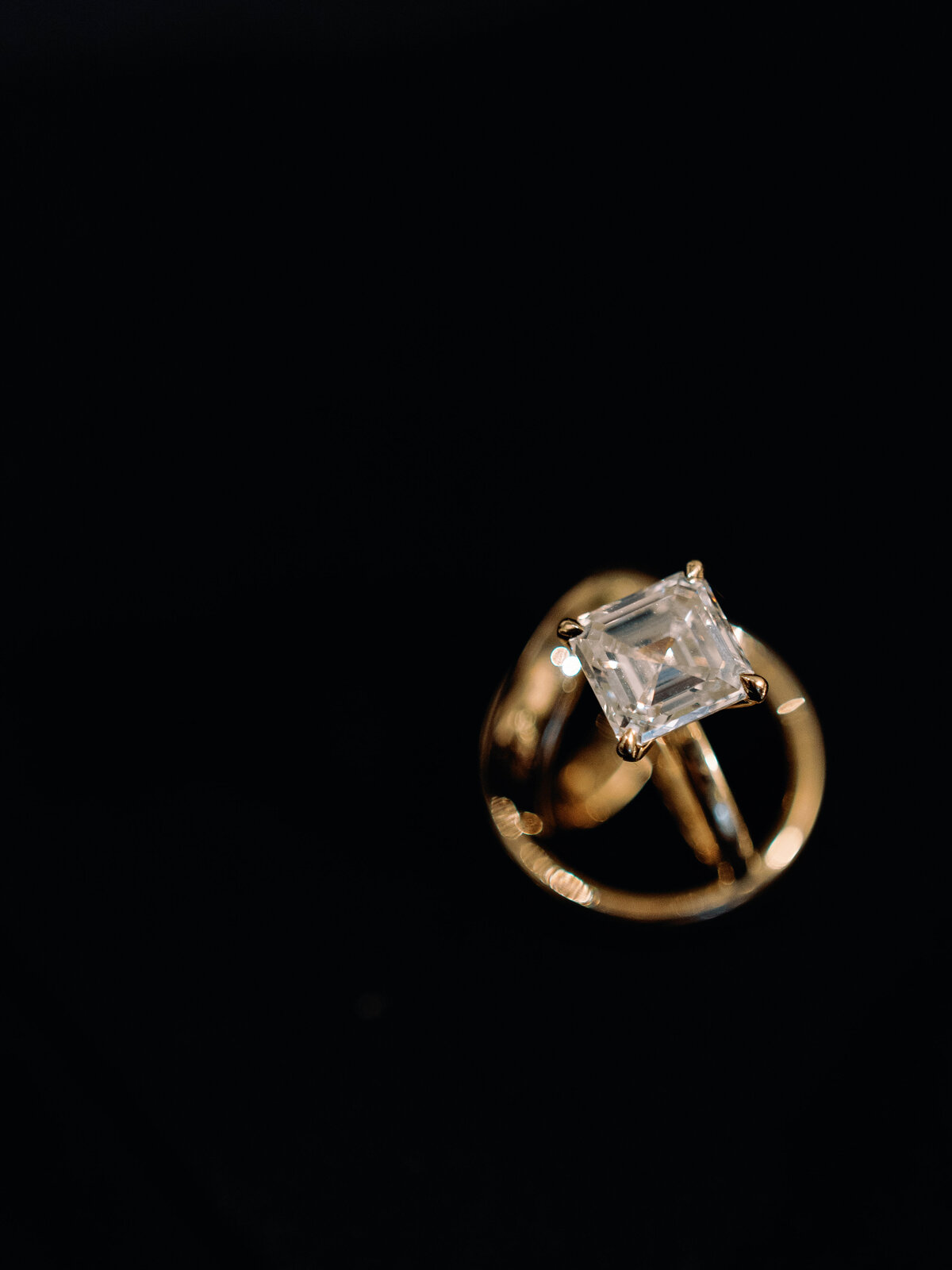 Editorial-style close-up of a gold engagement ring with emerald-cut diamond photographed against a black background during a space-themed wedding at the U.S. Space and Rocket Center in Huntsville, Alabama.