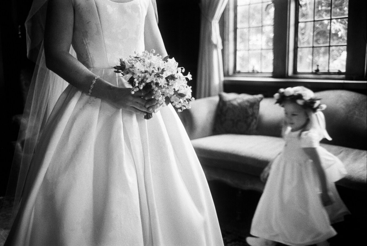A black and white image of a bride preparing to walk down the aisle with her flower girls nearby
