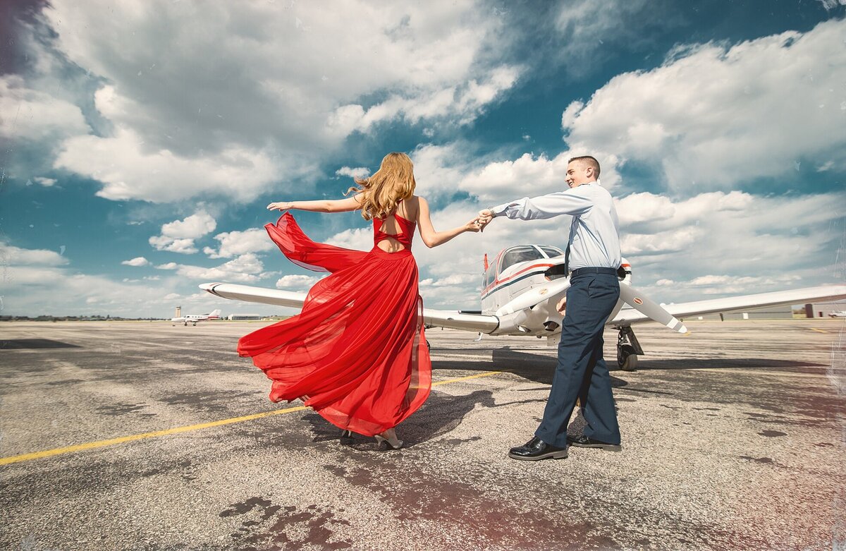 Man in military uniform  dancing with a girl in a red dress in front of an airplane