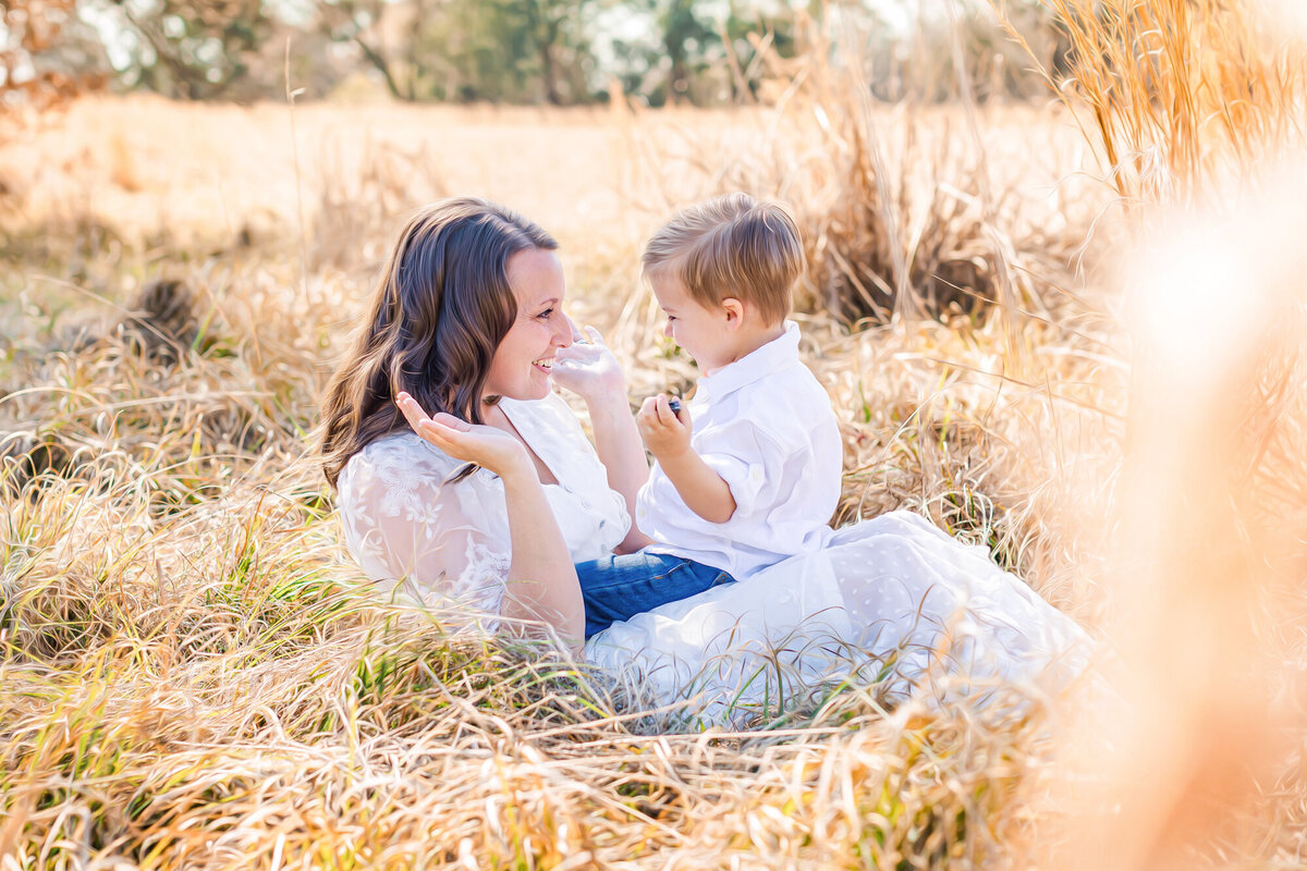 Mother and son sit in a field in Madison MS playing peek a boo during their motherhood session.