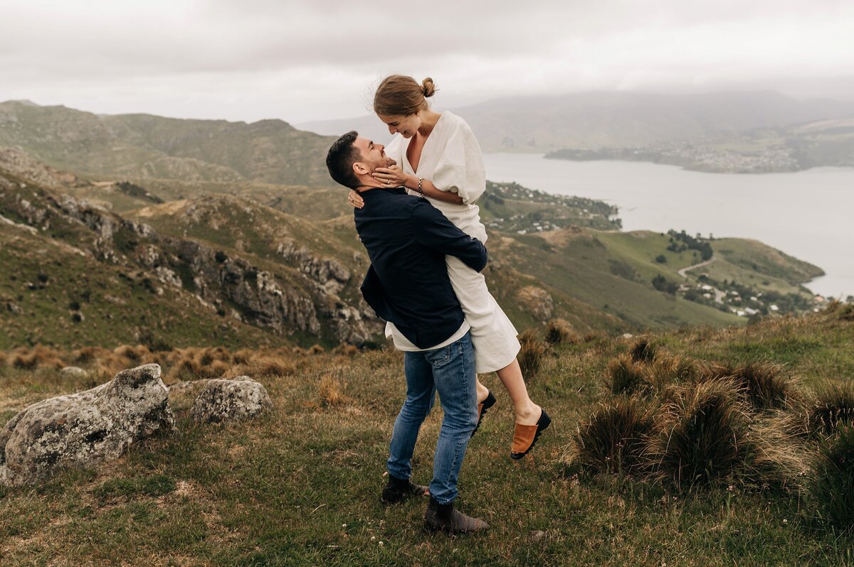 couple engaged white dress port hills christchurch wedding man picking up lady candid romantic view harbour lyttelton