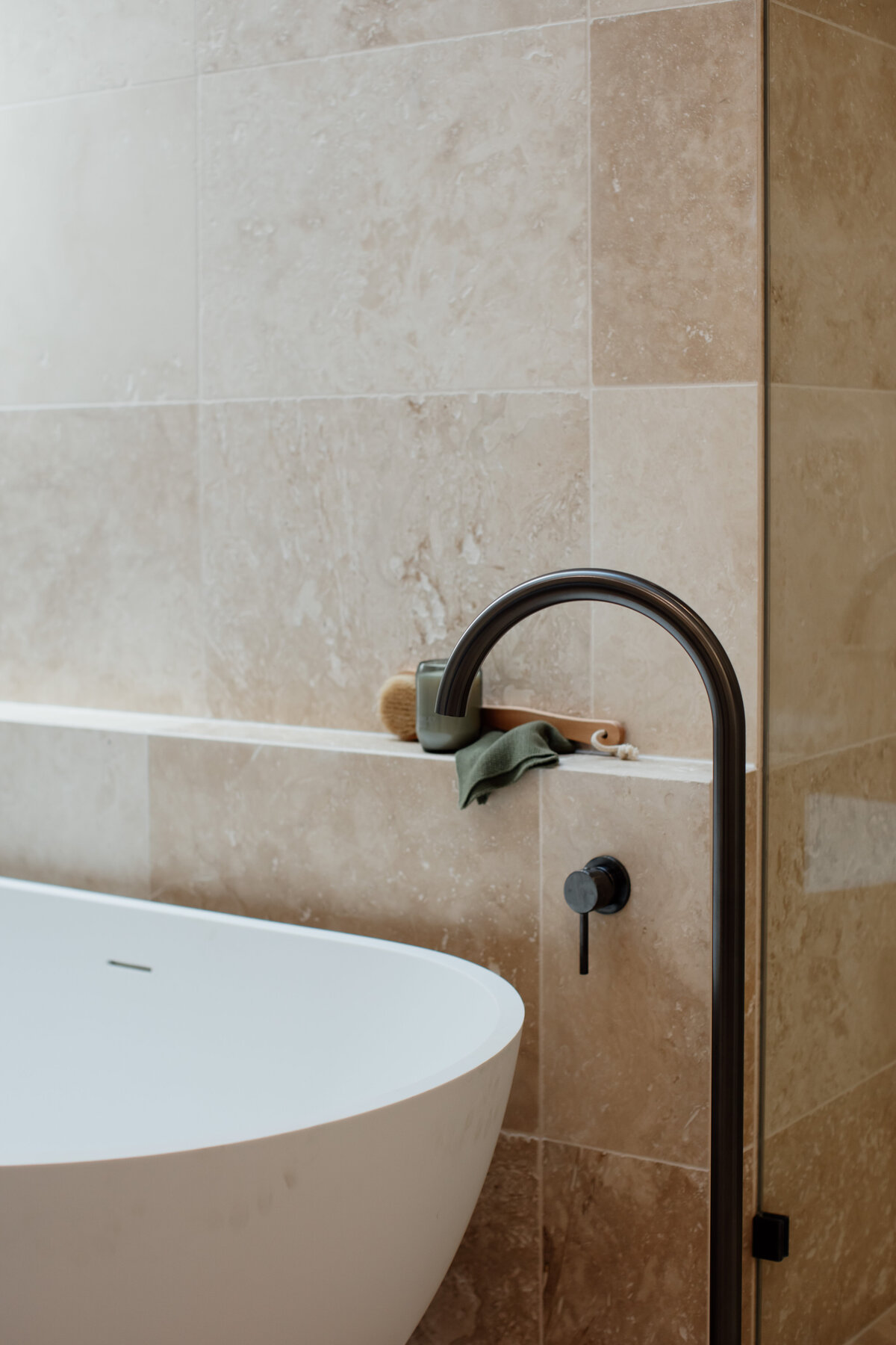Minimalist bathroom in a luxury home design with a white freestanding bathtub, dark faucet, and beige tiled wall, crafted by expert Newcastle kitchen and bathroom designers.