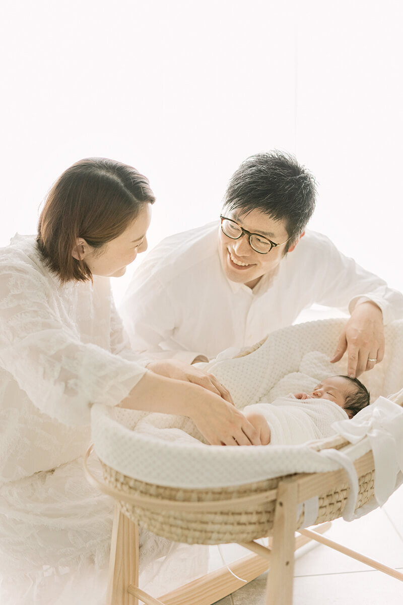 ママを笑顔で見つめているパパが印象的な、赤ちゃんと3人で写っている美しいナチュラル・ニューボーンフォト
