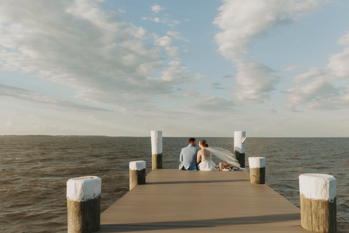 bride and groom sitting on harbor dock