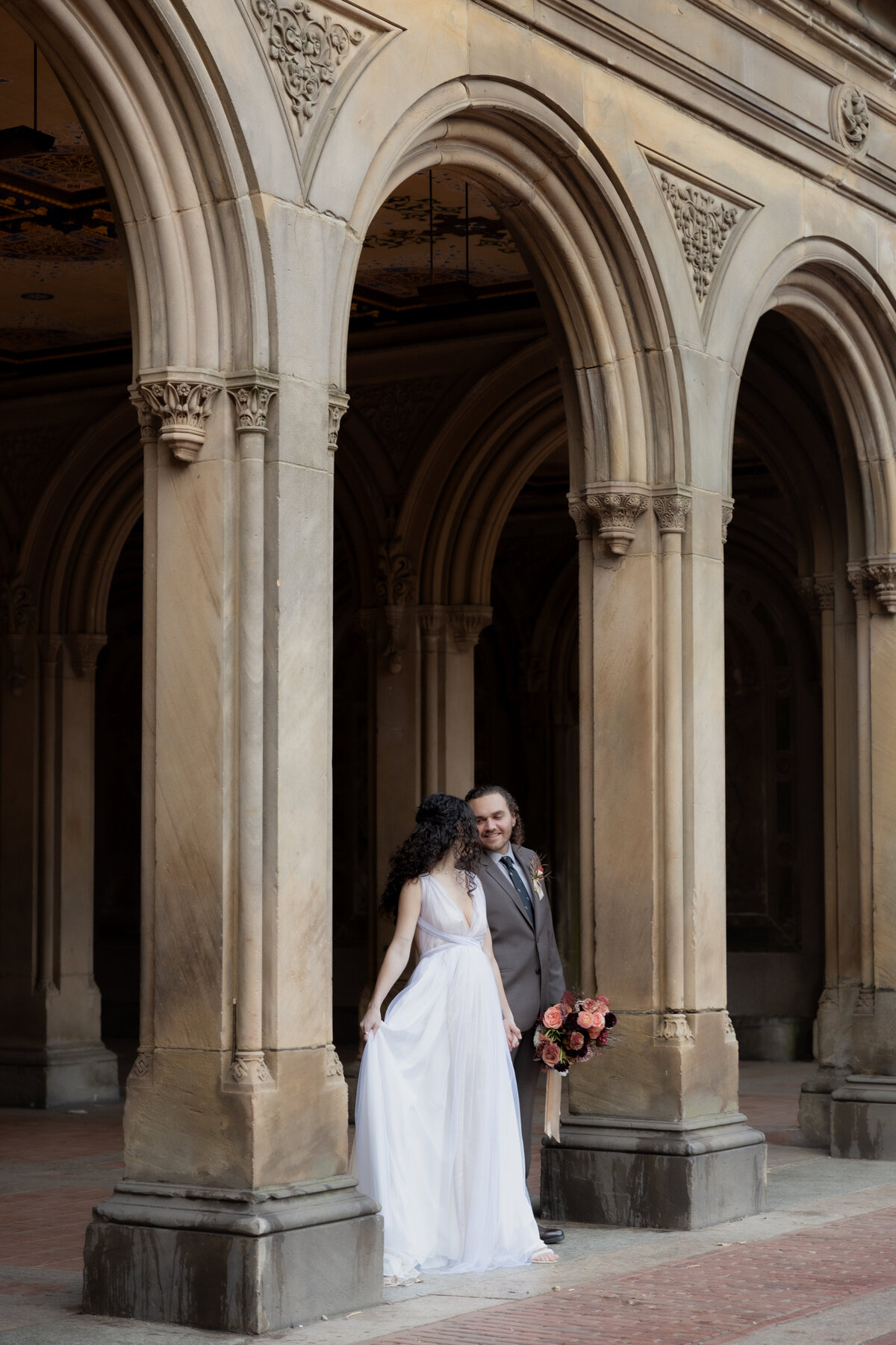 The couple walking hand-in-hand beneath historic archways in Central Park during their NYC elopement.