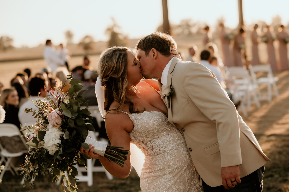bride leaning back as her groom kisses her at the end of their wedding ceremony aisle