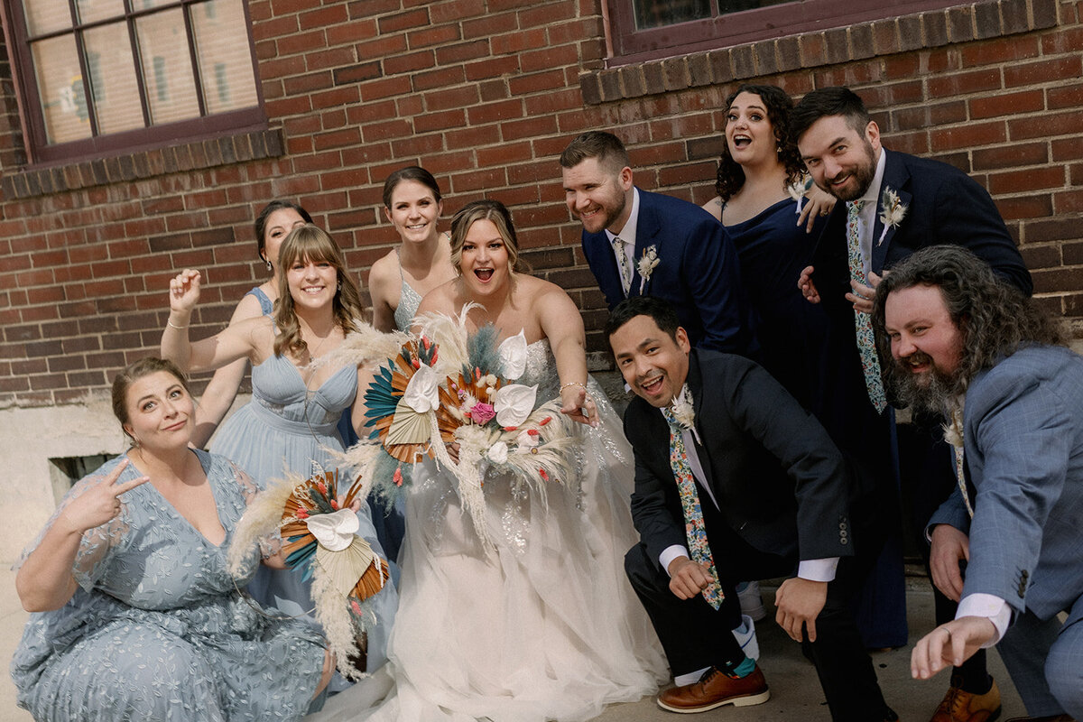 Bride and groom pose with their bridal party in blue and grey on their wedding day.