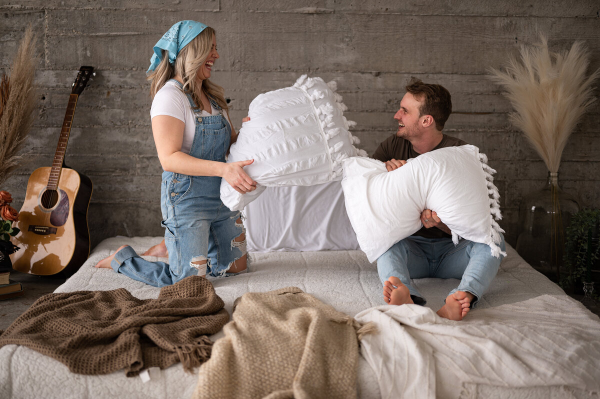couple have a romatic pillow fight during engagement session