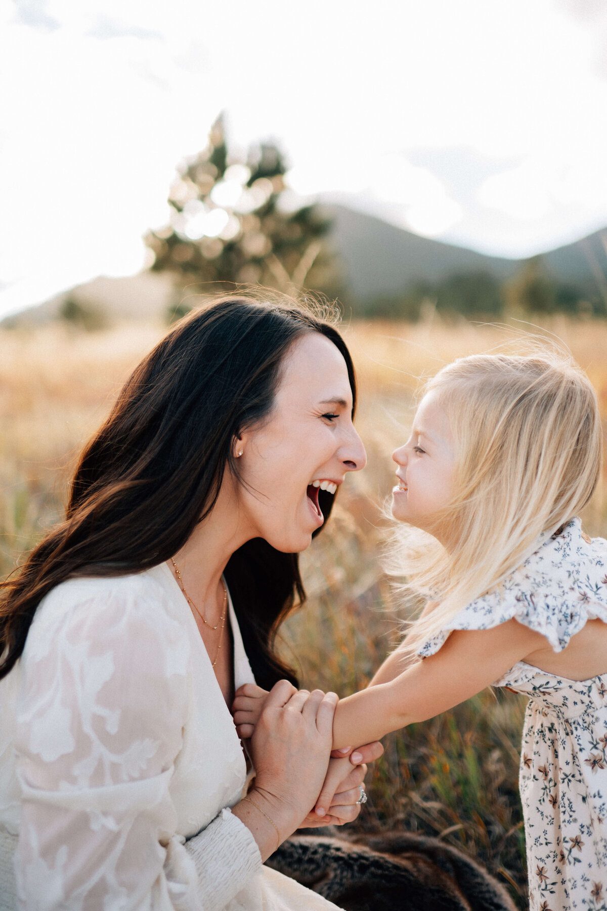 mom face to face with daughter holding her daughter's hands while they laugh with scrunch faces