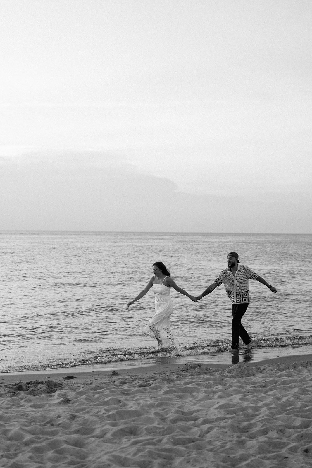 Playful photo of engaged couple running into Lake Michigan waves during sunset engagement photos