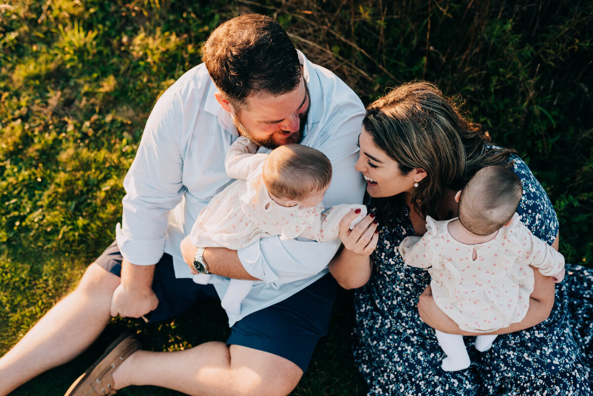 A mother and father play with their twin baby girls as they sit on the ground at sunset