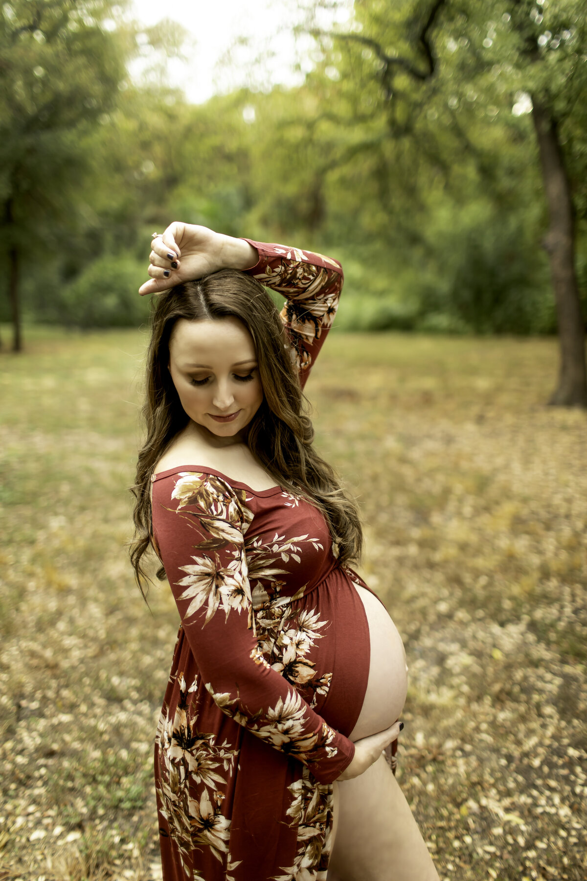 A vibrant maternity photo of the expectant mom in a red dress, standing confidently on a park path at Trinity Park, with sunlight filtering through the trees, captured by Chunky Monkey Photography.