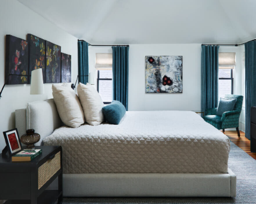 Interior designer in Boston created a primary bedroom design with custom drapery and teal blue pillows in a neutral space, balancing color with classic style.