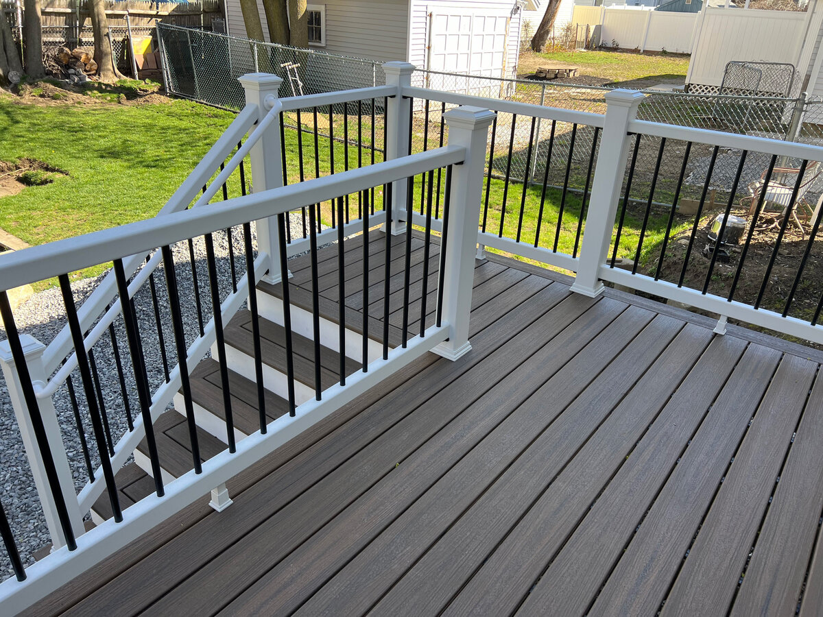 A corner stair set of a large deck in a back yard with white railings