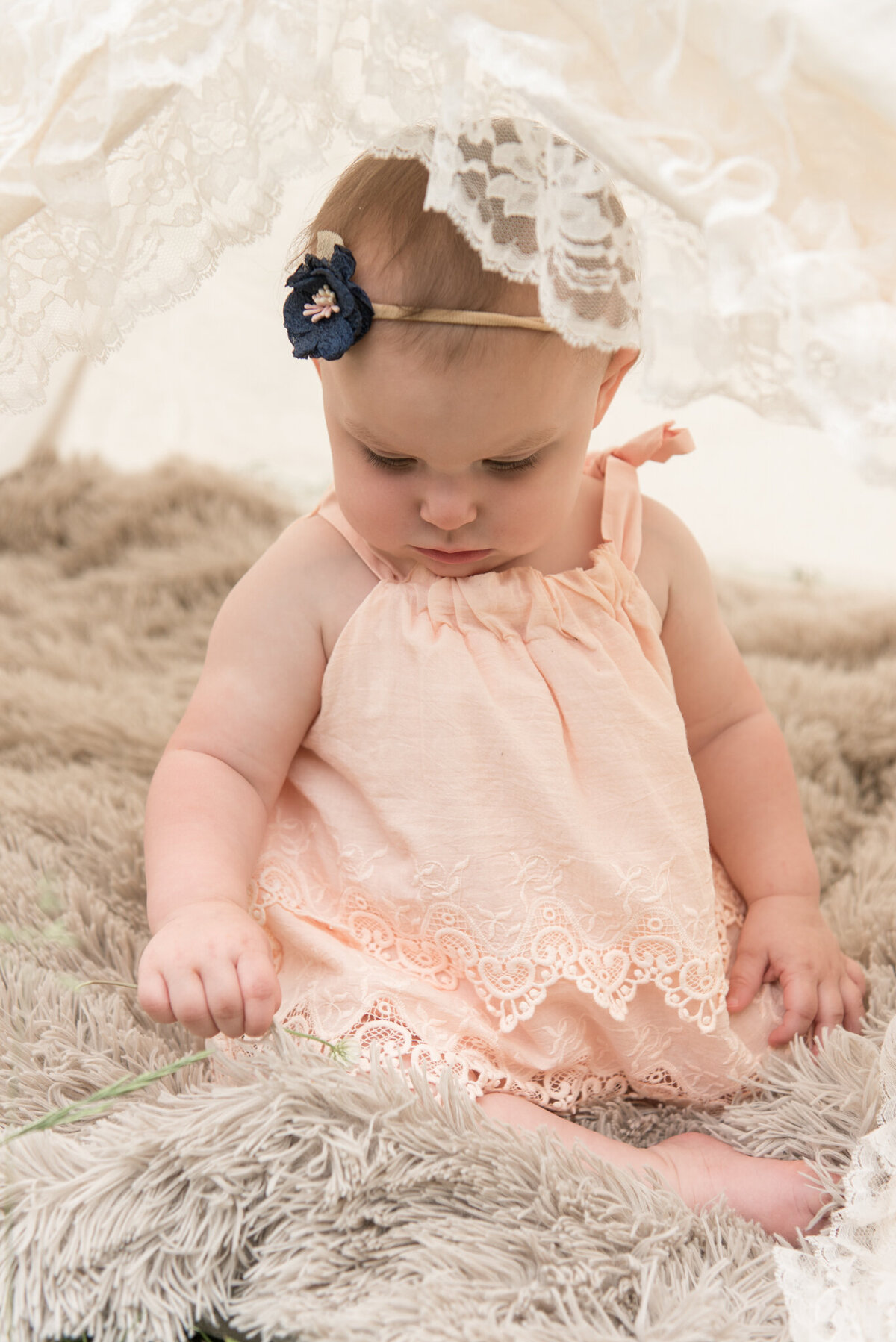 Little girl sitting in lace tent with blue headband and light pink romper
