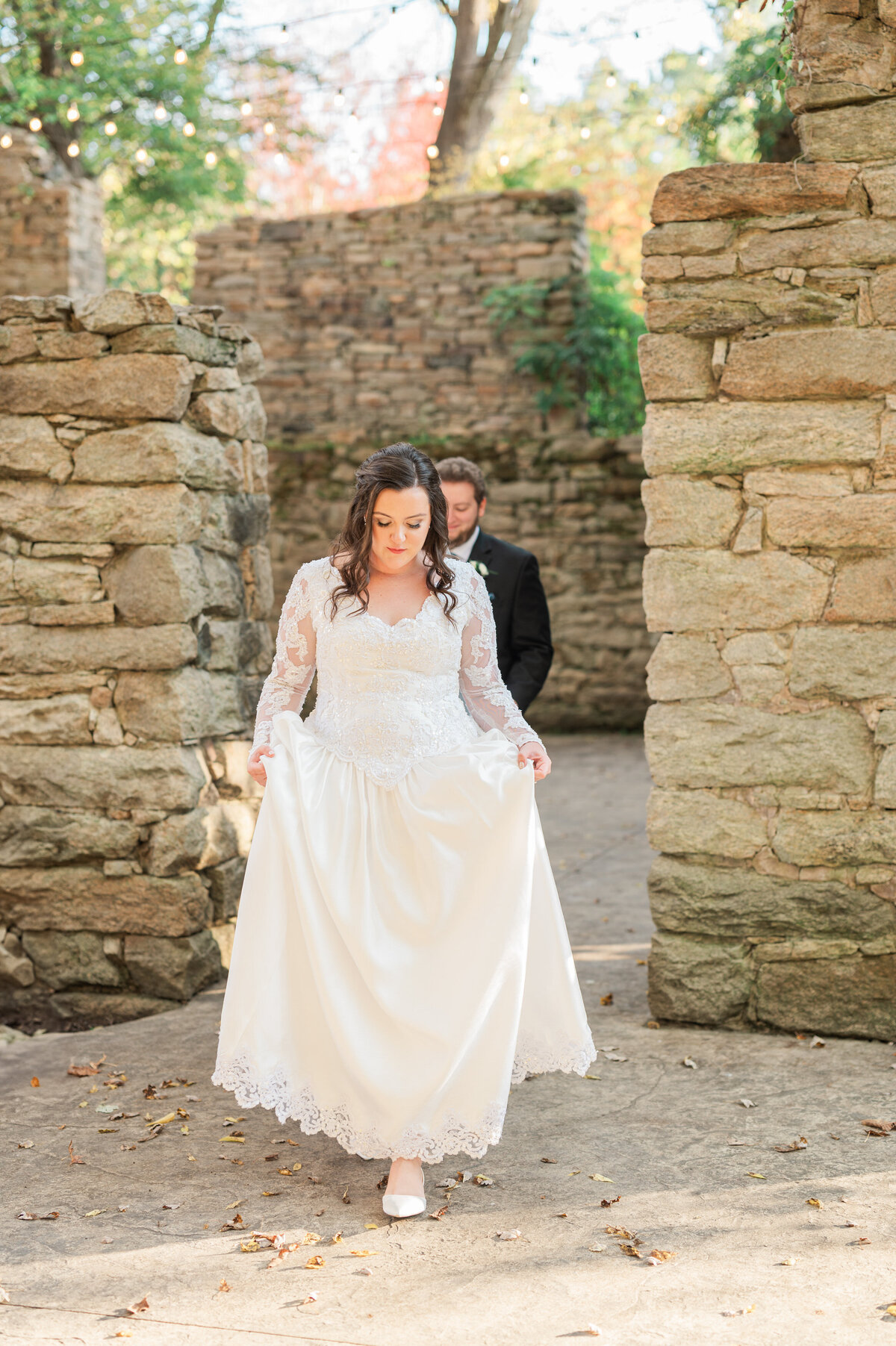 A person walking up behind their partner as she holds up the bottom of her wedding dress