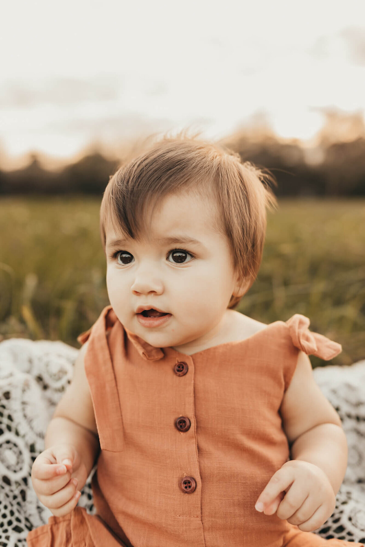 baby girl wears a rust romper for her birthday session outside for ally's photography