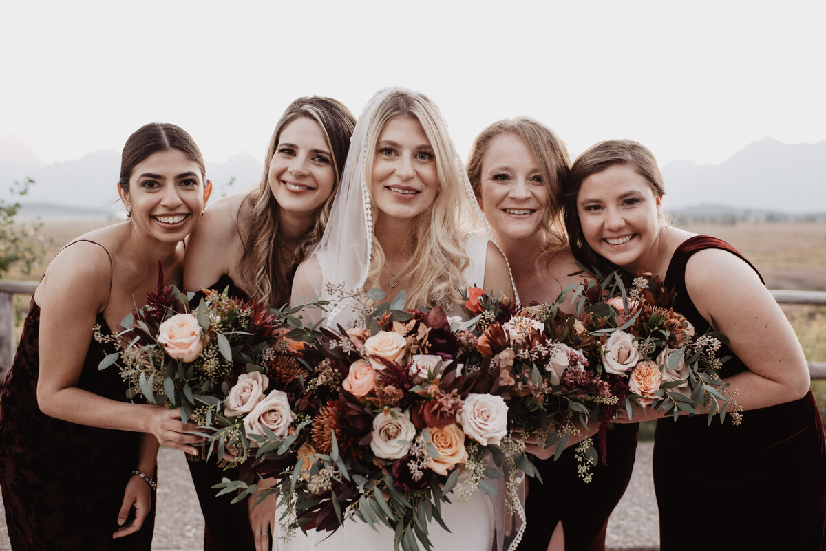 Photographers Jackson Hole capture bride smiling with bridesmaids holding bouquets