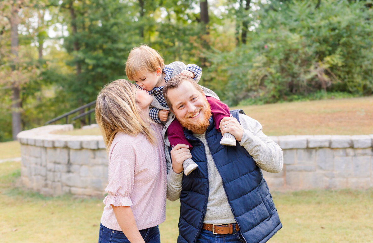 toddler boy on dad shoulder kissing mum in a park Atlanta GA