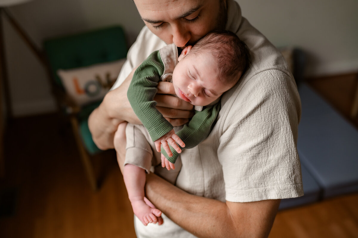 A father holds his newborn against his chest, wrapped in a romper, showcasing a tender, emotional connection in Ijamsville, MD
