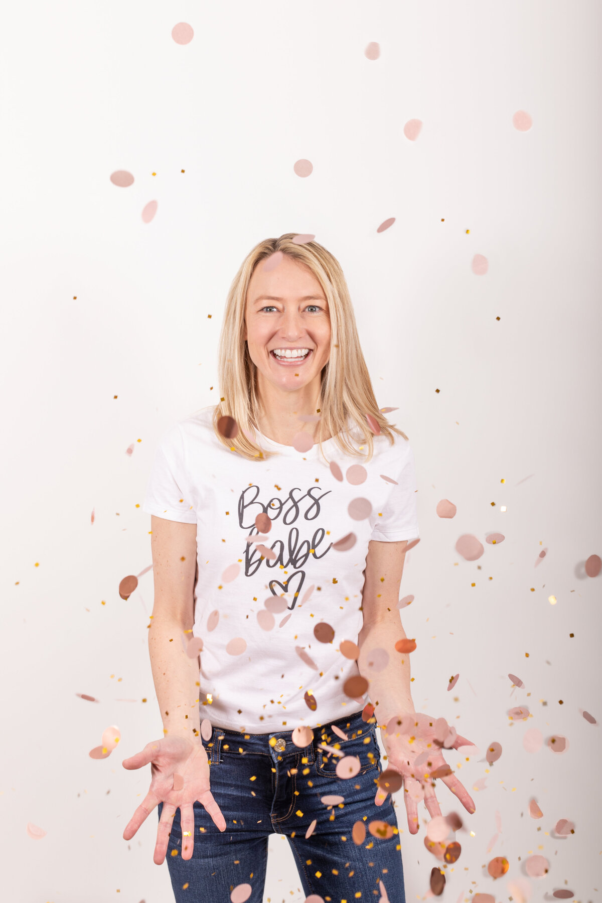 A confident woman wearing a “Boss Babe” tee tosses confetti with a big smile against a white backdrop—expressing empowerment and celebration in a playful brand photo.