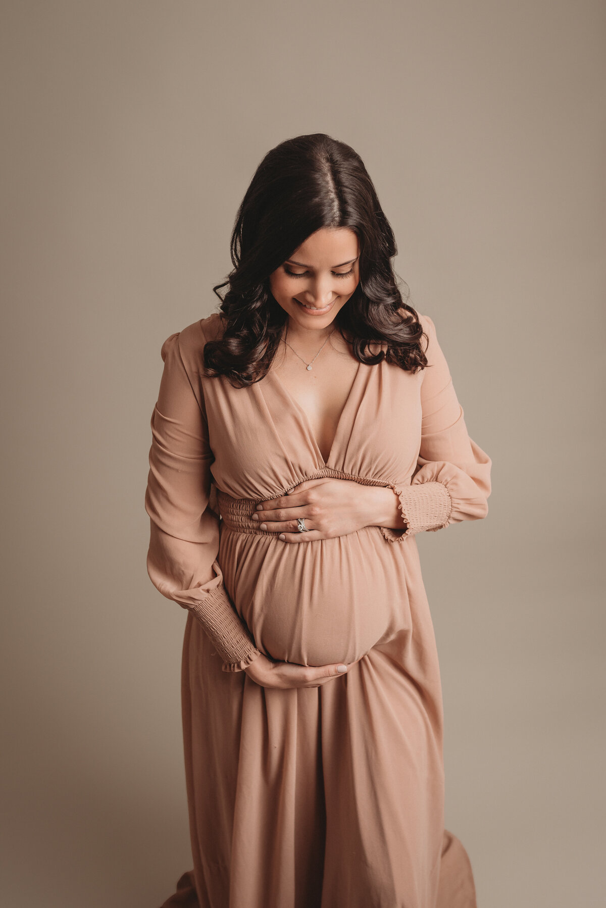 30 week pregnant woman wearing mauve long sleeve gown holding baby bump looking at her tummy