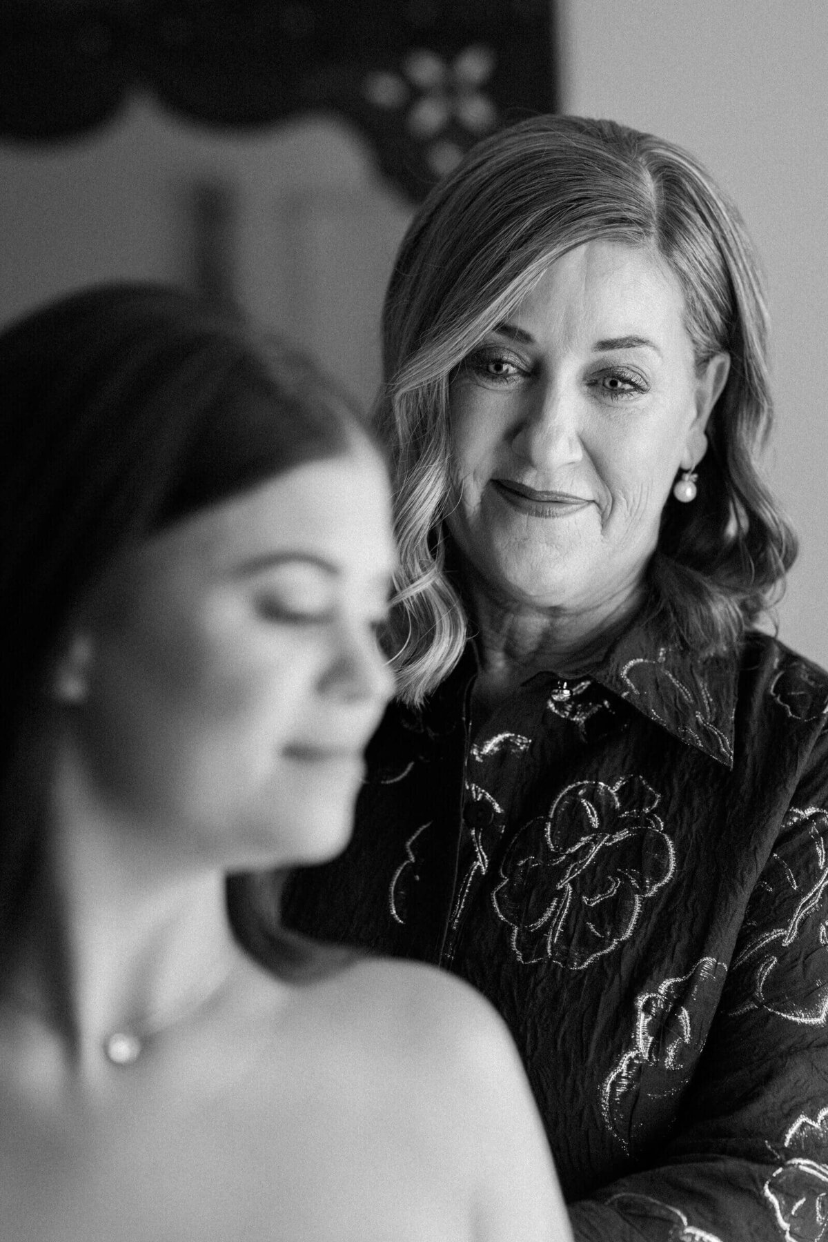 Candid black-and-white photo of a mother smiling proudly at her daughter as she gets ready on her wedding day at El Chorro in Scottsdale, Arizona.