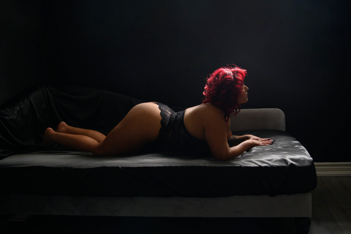 Red haired woman on stomach down on a bed with her butt up for her Toronto Boudoir Photography session.