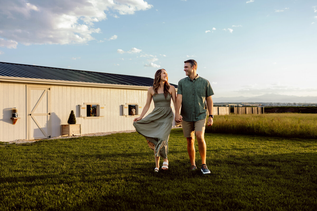 Husband and wife walking hand in hand on a farm on a summer day for their photo session in Denver