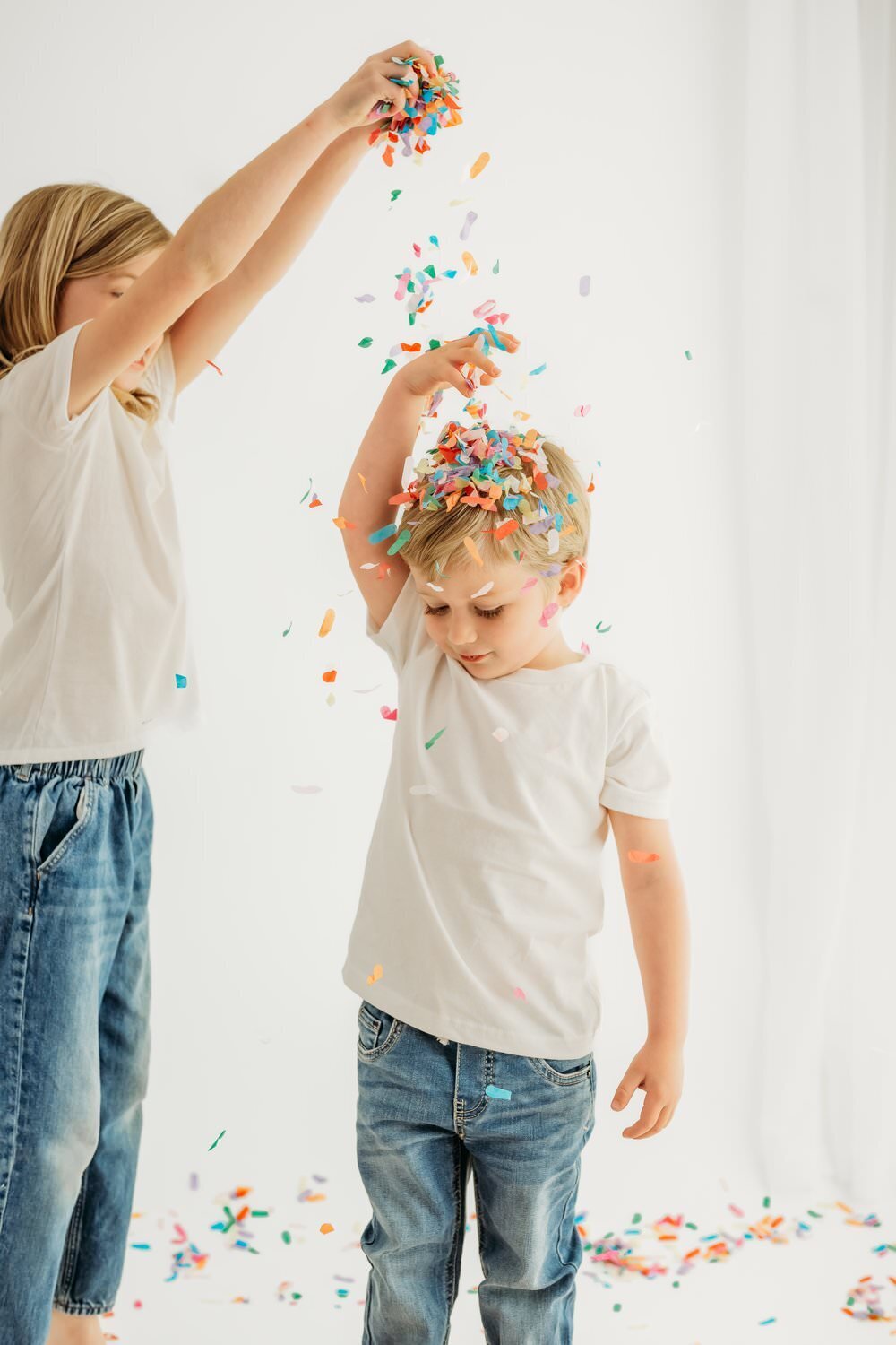 sister makes rainbow confetti fall on her brothers head.