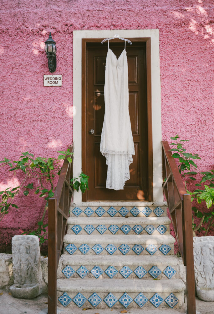 a wedding dress hanging on a pink doorway in Cozumel