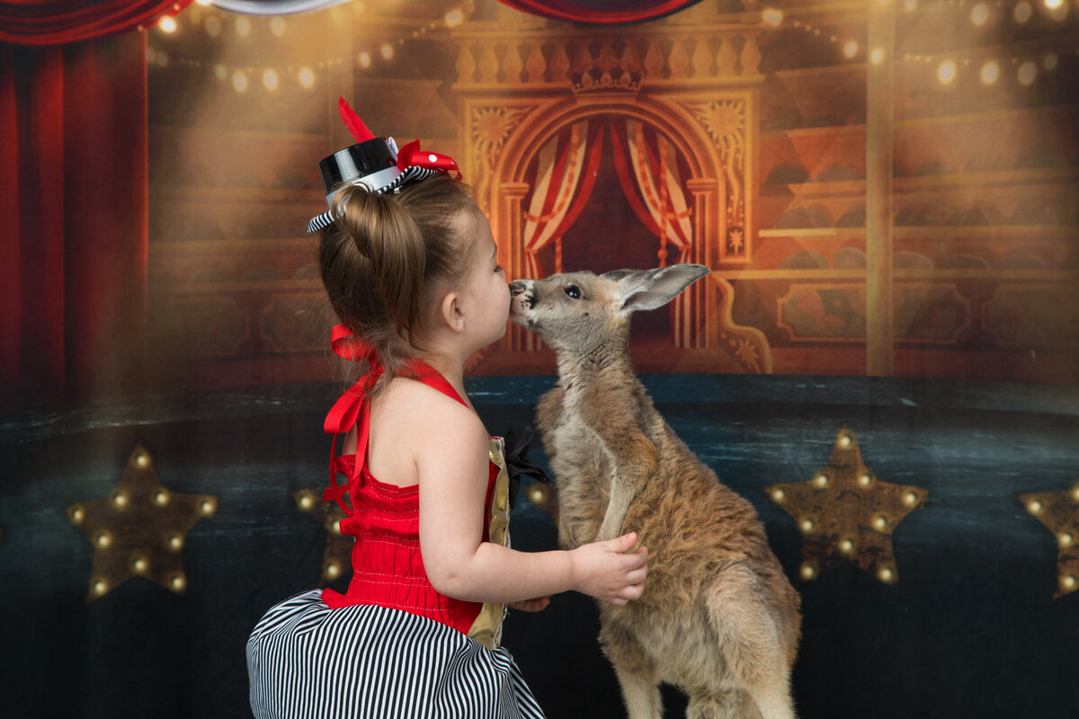 girl kissing a kangaroo in a circus theme studio portrait