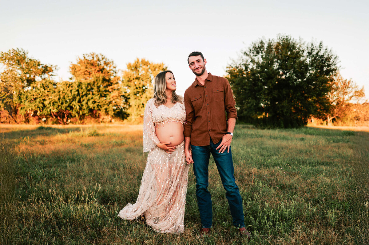 maternity photo of couple holding hands holding baby bump in field at sunset in field in Springfield MO