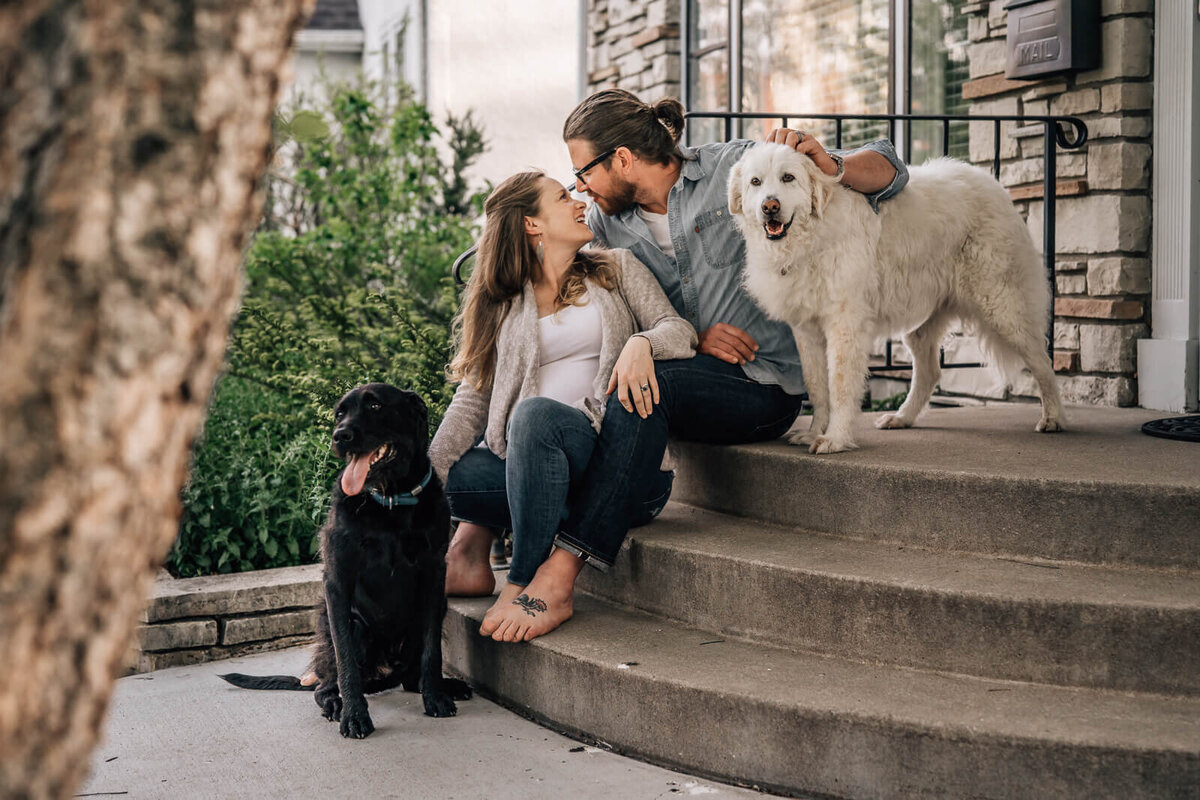 A pregnant couple sits on the front steps of their home with their two dogs during a shoot with Minneapolis maternity photographer, Kate Simpson.
