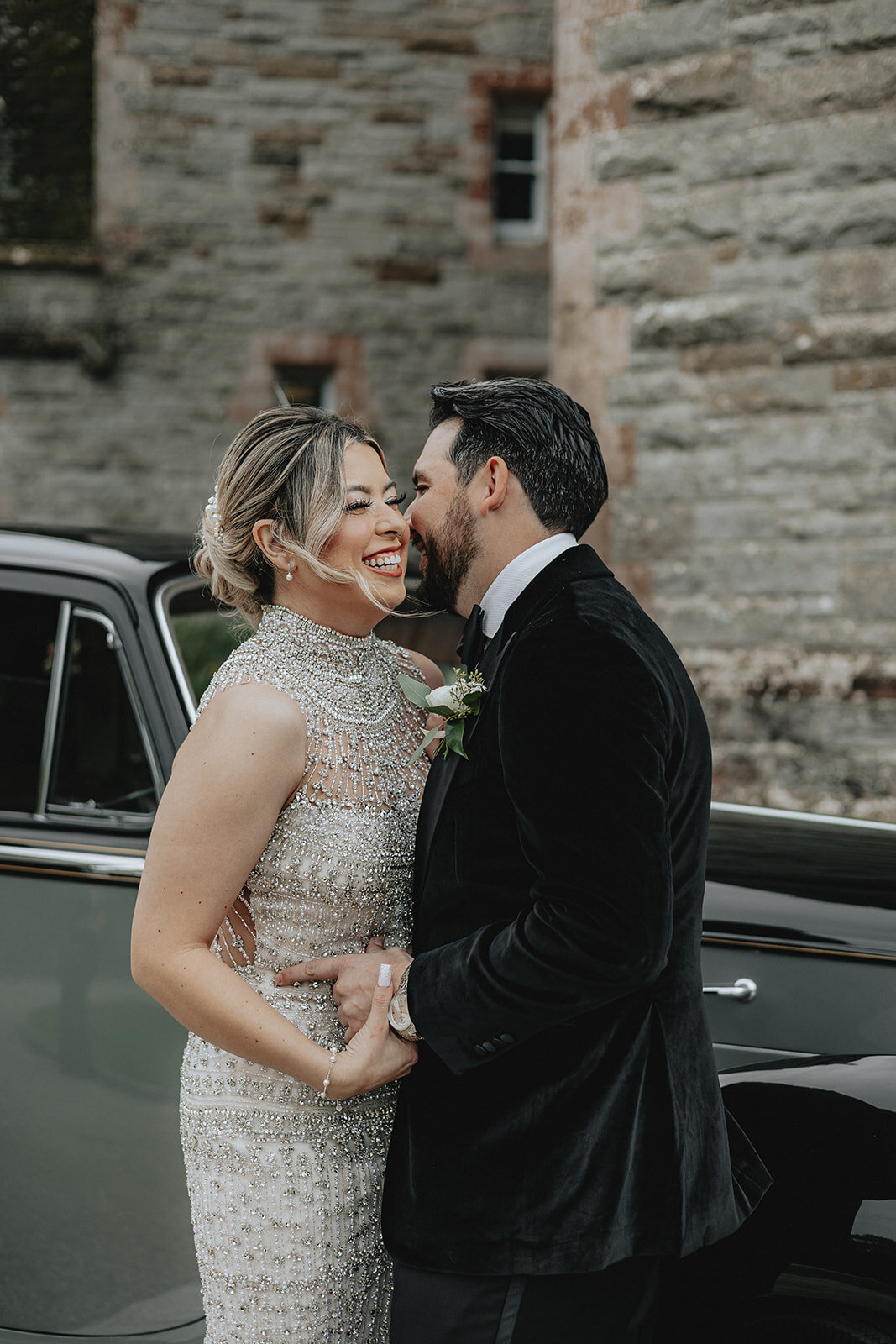 Bride and groom laughing holding each other in front of car