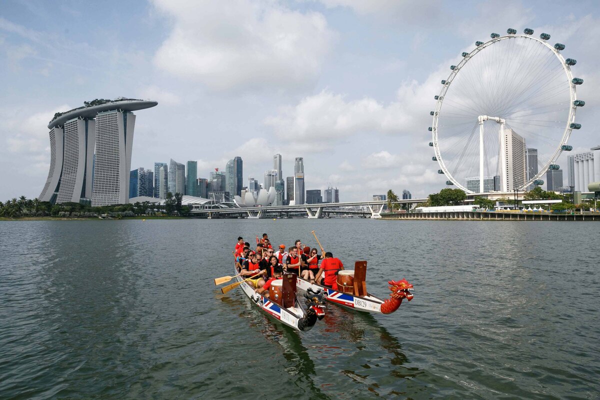 A group of attendees enjoys a boat rental with ferris wheel and Marina Bay Sands Hotel in background