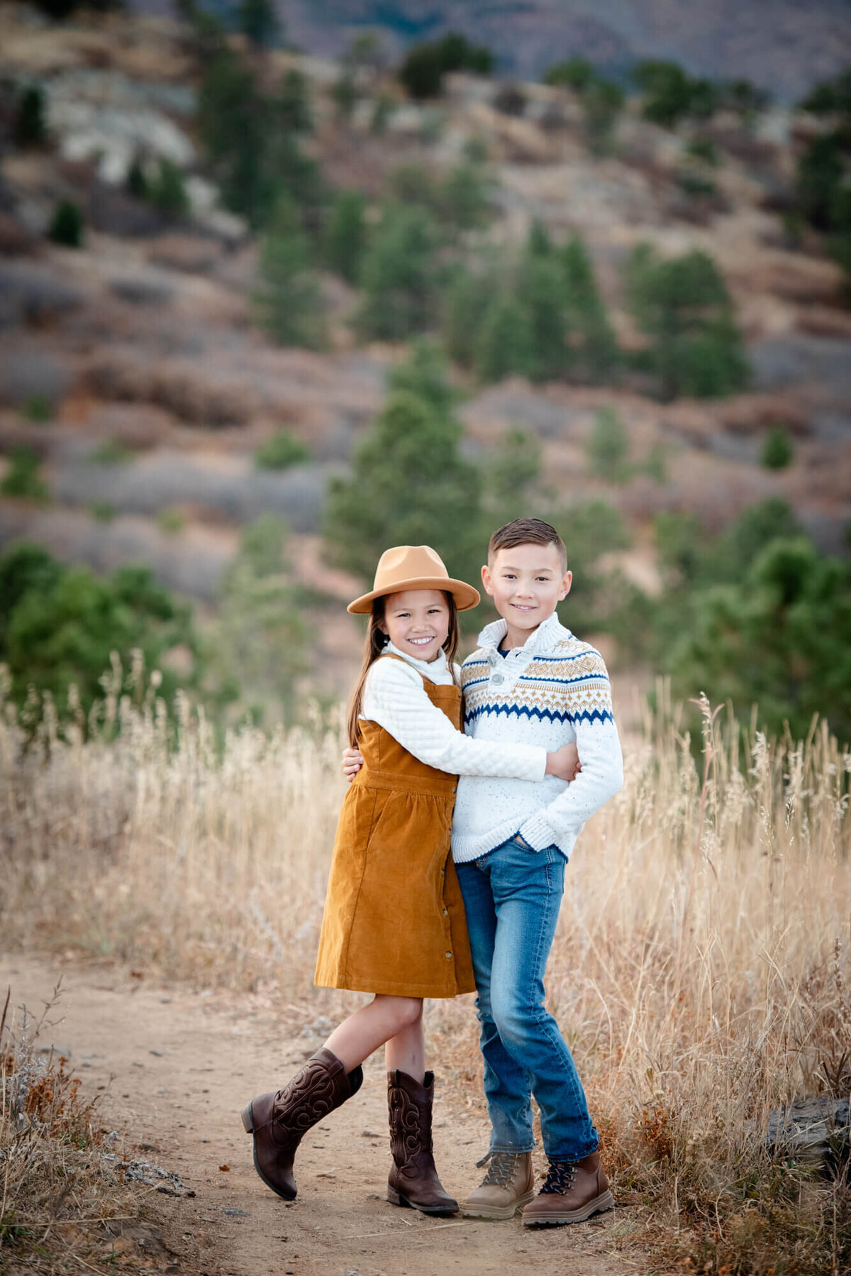 A young girl in an orange dress hugs her older brother while hiking on a trail