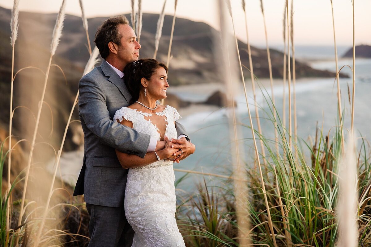 The bride and groom watch the sunset with Andrew Molera State Beach in the background.